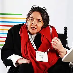 Abualghaib seated and wearing a white shirt, a black jacket, and a red scarf