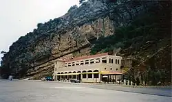 Two story stone structure built into the side of a cliff. The second floor has an outdoor balcony.