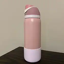 32 ounce Owala water bottle with silicone bottle boot. The bottle boot is silicone, a lighter shade of pink, and covers approximately the bottom quarter of the bottle. The lid is screwed on to the top with a closed flip top and carrying handle. "Owala" is written in recessed letters on a lighter pink ring on the bottom of the lid where it screws onto the bottle.