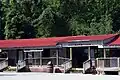 A historic market with red roof with a wooden "Ozark Folk Center" sign.