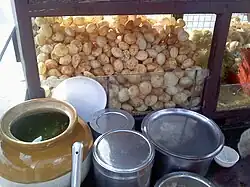 An uncovered jar of green flavoured water, in front of a pile of small puris
