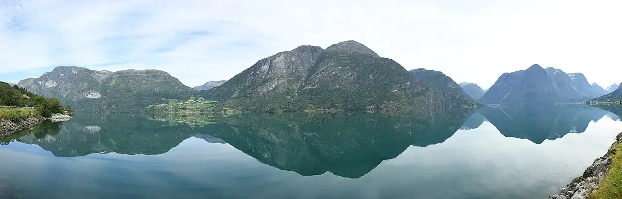 Panorama of Oppstrynsvatnet from the south side of the lake. The mountains Oppigardshyrna and Lægdekulen are visible in the center of the image. The village of Flo is located to the left of the two mountains. The mountain Hjellehyrna at the east end of the lake is visible on the right of the image.