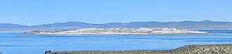A small, dark island rises above the calm, blue surface of a mountain-rimmed lake.