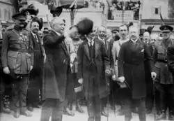 Paul Deschanel salue la foule de son haut-de-forme; derrière lui, les officiels se tiennent en rangs serrés.