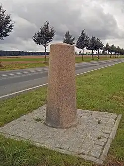 Photograph of a stone pilar that sits next to a road lined with trees