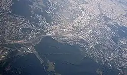 Aerial view of Penzing with Otto-Wagner-Spital near the top of the photo (three rows of big buildings), square-shaped Gerhard Hanappi Stadium downwards from it, and Baumgarten between them, with its sizable Baumgartner Cemetery.