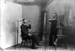 In this 1893 multiple-exposure trick photo, the photographer appears to be photographing himself. It satirizes studio equipment and procedures that were nearly obsolete by then. Note the clamp to hold the sitter's head still.