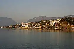 A collection of houses and other small buildings scatter the shore of a wide lake