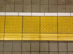 Tactile pavings installed on a platform at a Japanese train station. Horizontal tactile paving at the bottom indicates the 'inner' side, away from the rail tracks.