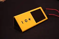 A triangular, yellow, music player with a black screen and three buttons in the shape of a -, o, and +