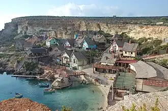 Colorful wooden buildings with whimsical architecture line a small cove with turquoise water, backed by steep rocky cliffs