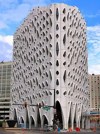 Exterior of a white color building featuring asymmetrical rounded multiple window and door openings, beside a traffic signal on a road under the blue and light cloudy sky
