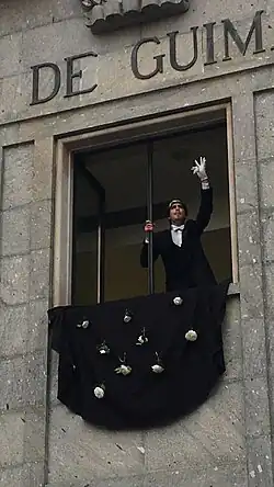 A young man in a suit, waving at a window