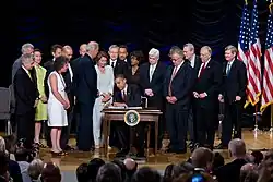 President Barack Obama signs the Dodd-Frank Act at a desk, surrounded by officials.