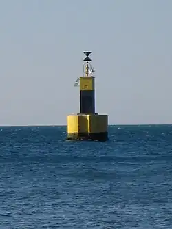 A wide base painted yellow supports a narrower pillar painted black on the bottom and yellow on top, with an hourglass-shaped marker on top.