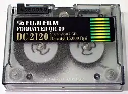 A QIC-80 tape; Magnetic tape is fed from a spool on the left, through a window, against a capstan, and onto a spool on the right. The spools are kept wound in sync by a rubber belt that presses against both spools and is moved by the capstan. A label identifies the brand, capacity, and other information about the tape.