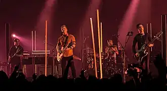 Queens of the Stone Age in 2017. Left to right: Dean Fertita, Josh Homme, Jon Theodore, and Michael Shuman. Not pictured: Troy Van Leeuwen.