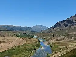 The Neuquén River, twisting and rather narrow, runs through Manzano Amago. There are hills in the distance.