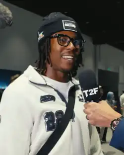 Headshot of Shaheed wearing glasses, a blue Seahawks beanie, and a white Seahawks jacket