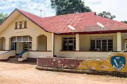 A yellow two-storey building behind a fence with the seal of Kikwit