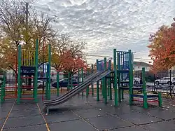 Playground equipment with streets and parked cars in the background.