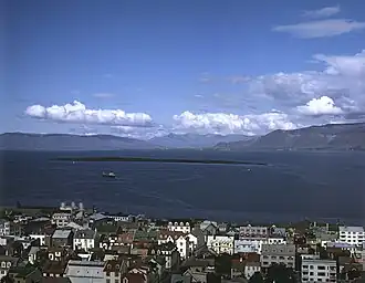 View of Engey island seen from a hill in Rekyjavik. There are buildings in the foreground and the long, thin island in the sea.