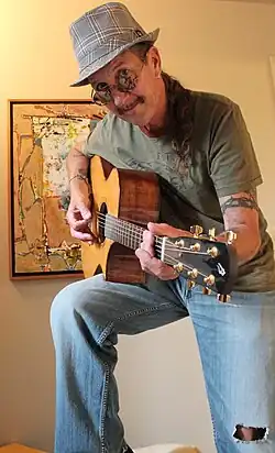 Richard Fagan poses with Todd Cerney's guitar in front of painting by Gloria Newton