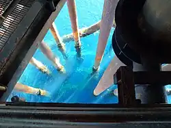 Steel subsea riser pipes descending into seawater beneath the deck structure of an offshore oil platform.