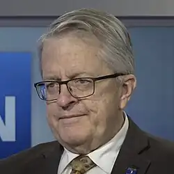 Headshot of Burton in a suit wearing glasses