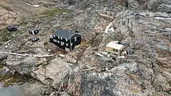 Areal view of a two story house and three small wooden houses on a rocky shore