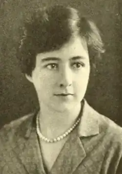 A young woman with pale skin and short dark hair, wearing a strand of pearls