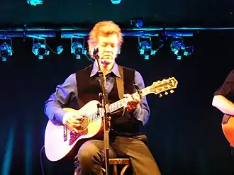 Singer Rodney Crowell, seated on a stool and playing an acoustic guitar