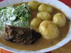 Rolada covered in sauce with potatoes and salad on the side