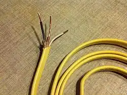 A photo of NM cable with a stripped end and a yellow coloured PVC sheath.