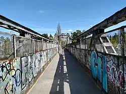 Pictured is a bridge, with significant amounts of grafitti on both sides. There is a solid wall that transitions into chainlink on either side.