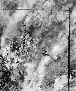 An overhead view of a bomber aircraft, flying over a pall of smoke