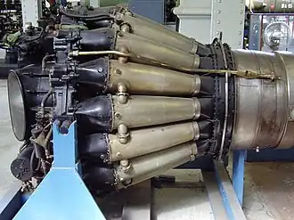 de Havilland Goblin with sixteen straight-through combustion chambers. Each consists of a flame tube enclosed in a pressure-tight outer casing. They are connected by tubes which balance the pressure and propagate the flame during start from the two tubes with igniters one of which is shown on a top tube.[87]