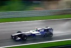 A dark blue and white Formula One being driven at high speed on a racing circuit