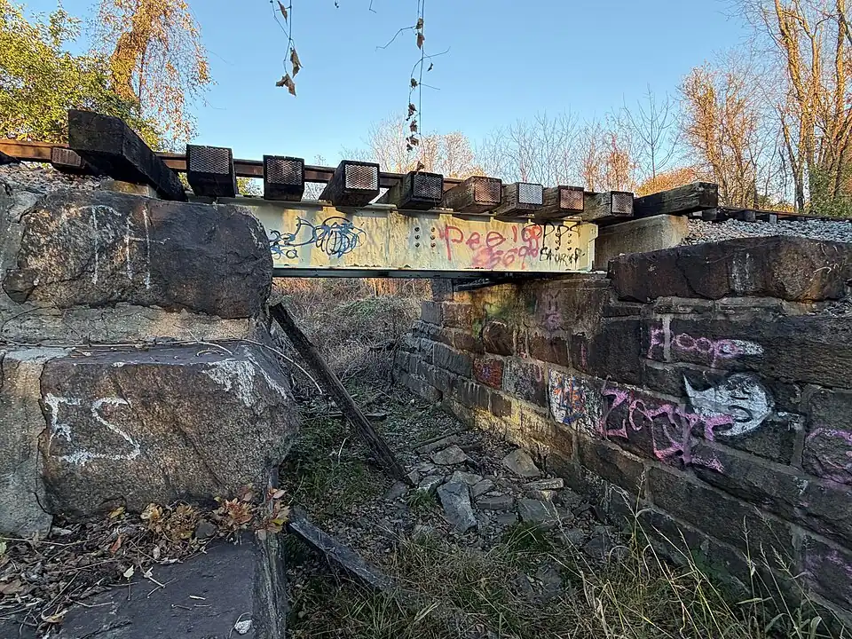 riveted plate girder bridge that crosses a smaller subsection of the Chester Creek , which was dried up at the time of capture. Positioned just behind West Chester Rustin High School.