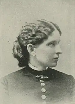 B&W portrait photo of a young woman wearing a dark, high-collared blouse with her hair in an up-do.