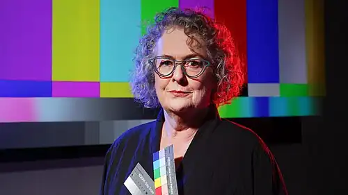 Media release photograph of Süsstrunk holding color swatches with a color-bars display in the background.