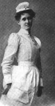 A white woman wearing a nurse's uniform, standing