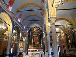 A view of the inside of the cathedral which features high ceilings and colorful walls. There are white pillars and arches throughout. A variety of artwork is displayed on the walls.