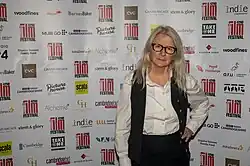 stylish woman with long grey hair in front of a cambridge film festival sponsors board