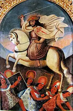Painting of a white man with a beard in a white mantle with a red Santiago cross in a pilgrim hat surrounded by light rays brandishing a sword. He rides a white horse charging over 6 native warriors.