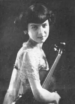 A girl with light skin and dark hair cut in bangs, holding a violin