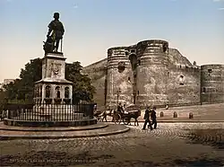 Photo of a paved square with a statue at its center, Angers Castle in the background; two small horse-drawn carriages circle the statue.