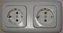 Schuko outlets manufactured by Busch-Jaeger Elektro. The right socket has protective shutters (gray in color) and the left does not.