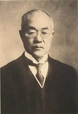A black and white photo of an older man in a suit and glasses looking right