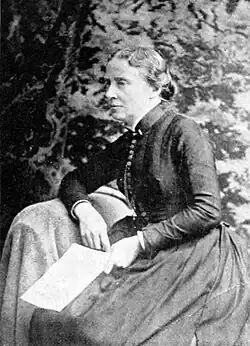 19th-century B&W portrait photo of a woman with her hair in an up-do, wearing a dark, fitted blouse.